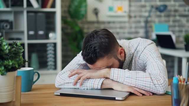 バロンチェア購入後に後悔し、ノートパソコンの上に頭を伏せる男性ユーザー