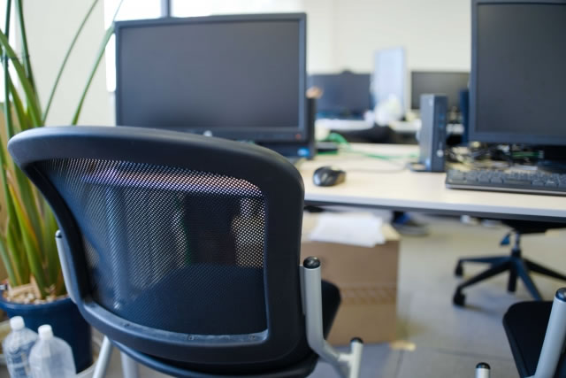 オフィスのデスクに並ぶパソコンとメッシュチェア