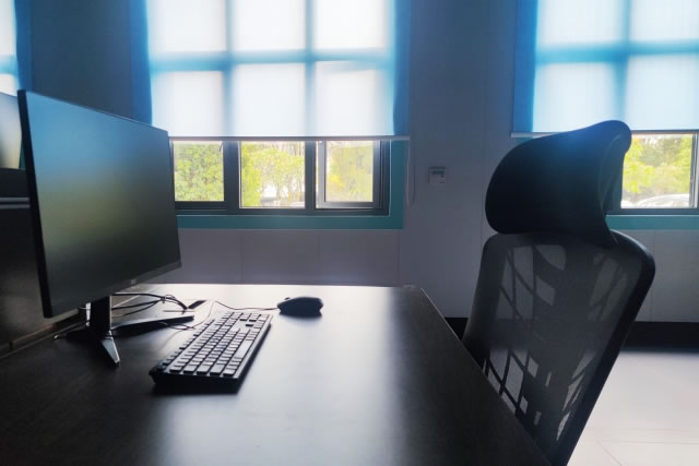 オフィスの机に設置されたパソコンと椅子、窓から光が差し込む様子