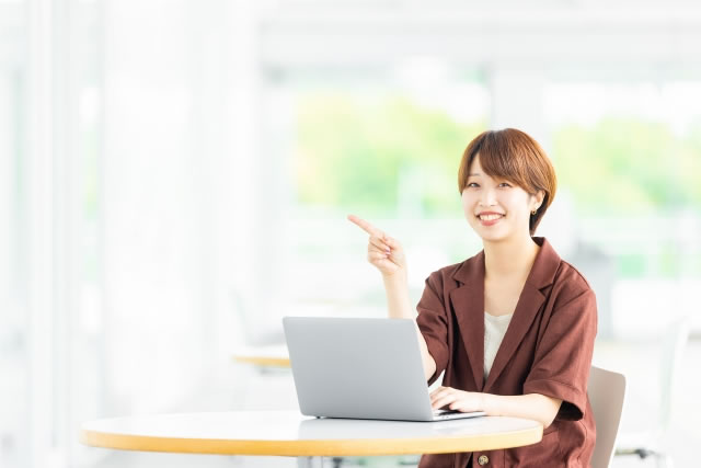 ノートパソコンを操作しながら指をさして笑顔を見せる女性